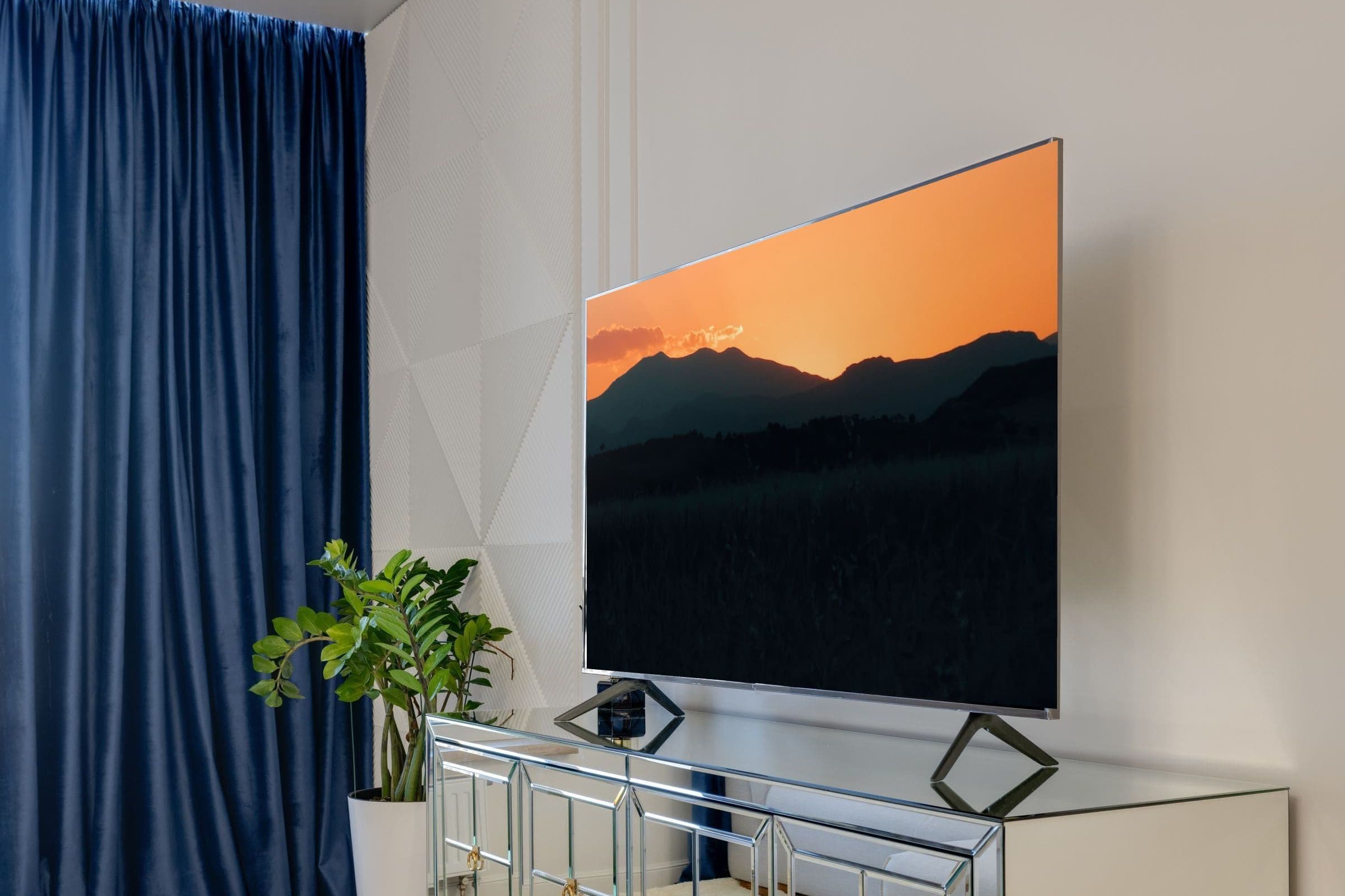 Grand téléviseur dans un salon moderne affichant un coucher de soleil sur des montagnes